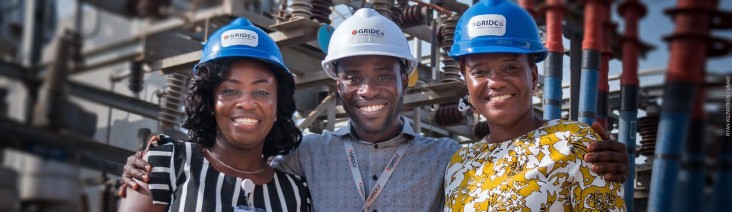 Three GridCo technicians pose in front of an electric power station