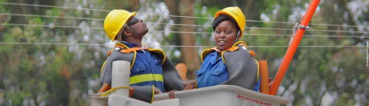 Two power line technicians—one male, one female—in their safety gear stand in a lift, preparing to work on power lines during a training exercise