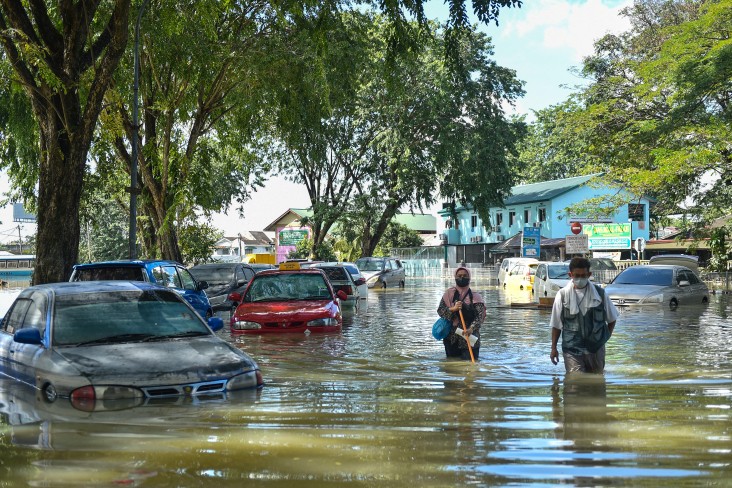 People walk past cars partially submerged in floodwaters in Shah Alam, Selangor