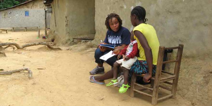 A field worker speaks with a woman holding a child.