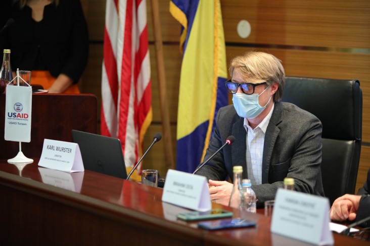 A man seated at a table speaks into a microphone.